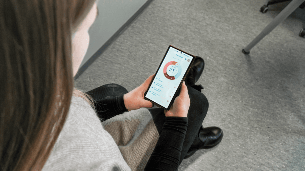 Henkilö katsoo älypuhelimeltaan Wilfa ilmalämpöpumppujen etäohjaussovelluksen kaltaista sovellusta.